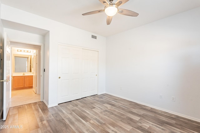 unfurnished bedroom featuring baseboards, visible vents, ceiling fan, light wood-style floors, and a closet