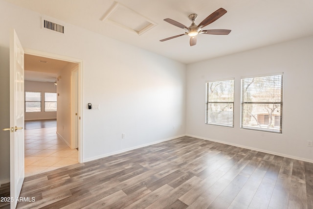 empty room featuring ceiling fan, wood finished floors, visible vents, baseboards, and attic access