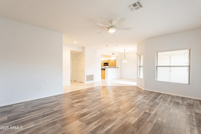 unfurnished living room with light wood-type flooring, baseboards, visible vents, and a ceiling fan