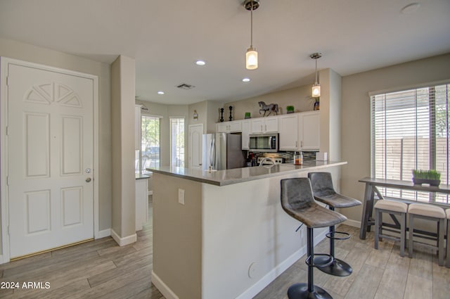 kitchen featuring pendant lighting, light hardwood / wood-style flooring, a kitchen bar, appliances with stainless steel finishes, and white cabinets