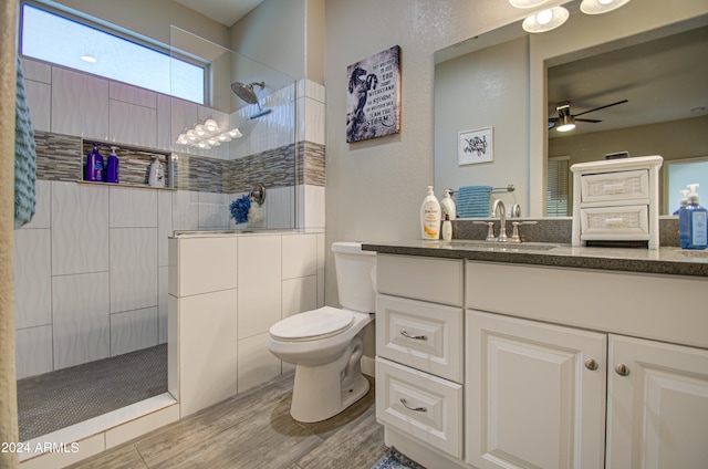 bathroom with toilet, wood-type flooring, tiled shower, ceiling fan, and vanity