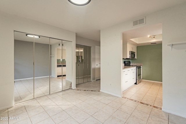 kitchen with stone countertops, stainless steel appliances, white cabinetry, and light tile patterned flooring