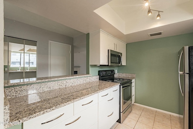 kitchen featuring a raised ceiling, light stone counters, white cabinetry, and appliances with stainless steel finishes