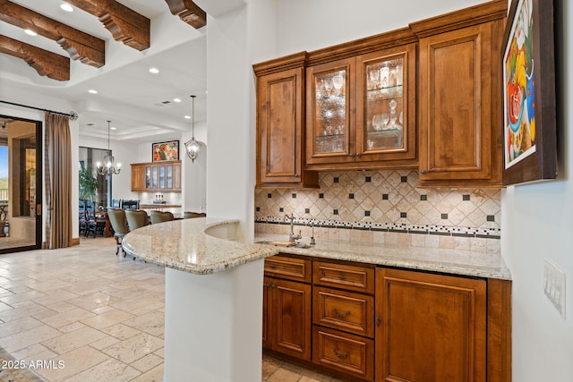 kitchen with hanging light fixtures, a notable chandelier, light stone countertops, and backsplash