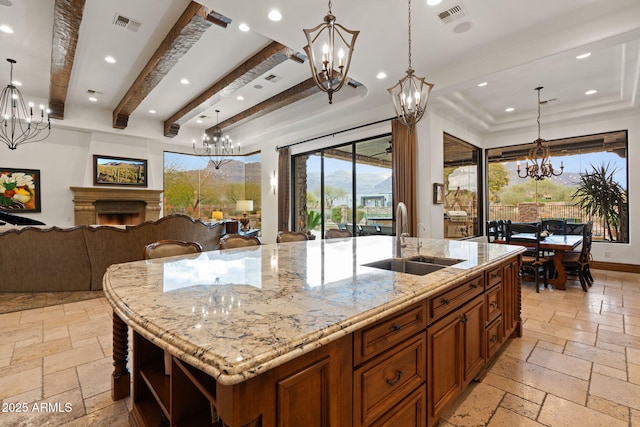 kitchen featuring sink, an inviting chandelier, light stone countertops, decorative light fixtures, and a large island with sink