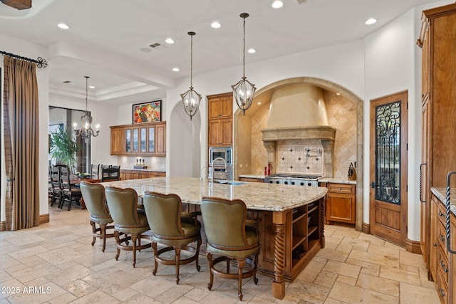 kitchen featuring a spacious island, sink, light stone counters, decorative light fixtures, and stainless steel microwave