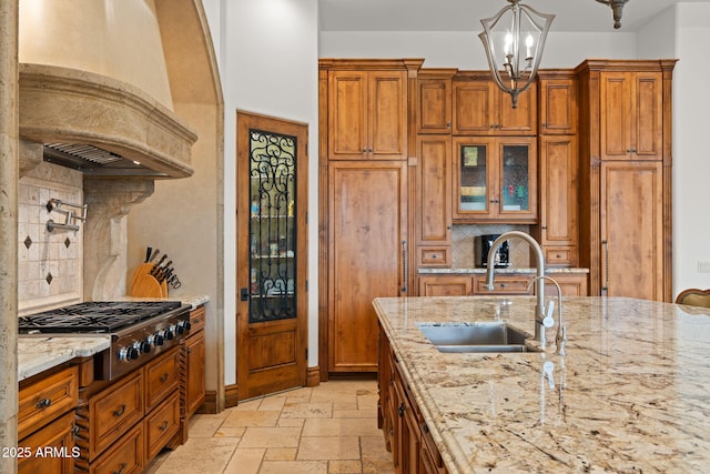 kitchen featuring sink, light stone counters, decorative light fixtures, custom exhaust hood, and stainless steel gas stovetop