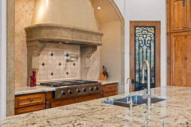 kitchen featuring sink, backsplash, light stone counters, stainless steel gas cooktop, and custom exhaust hood