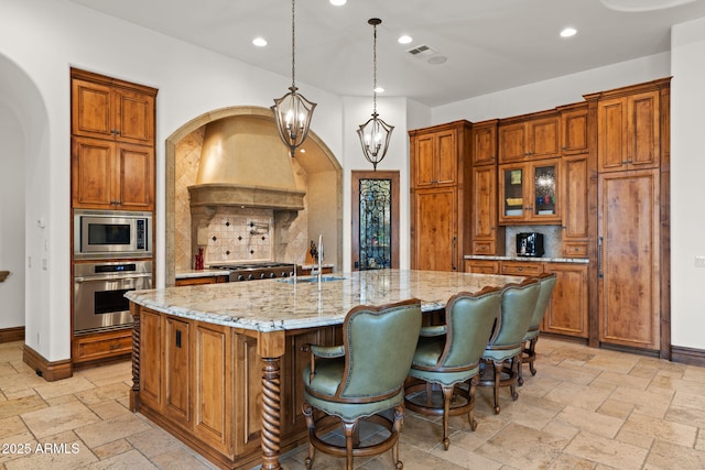 kitchen with sink, appliances with stainless steel finishes, a spacious island, light stone counters, and decorative light fixtures