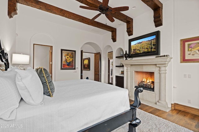 bedroom featuring beam ceiling, ceiling fan, hardwood / wood-style floors, and a fireplace