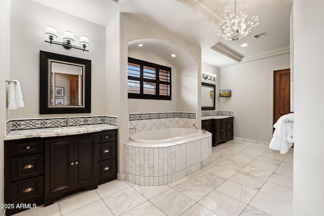 bathroom with vanity, a relaxing tiled tub, and a chandelier