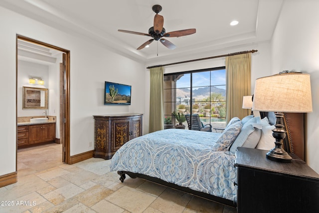 bedroom featuring ceiling fan, ensuite bath, a tray ceiling, and sink