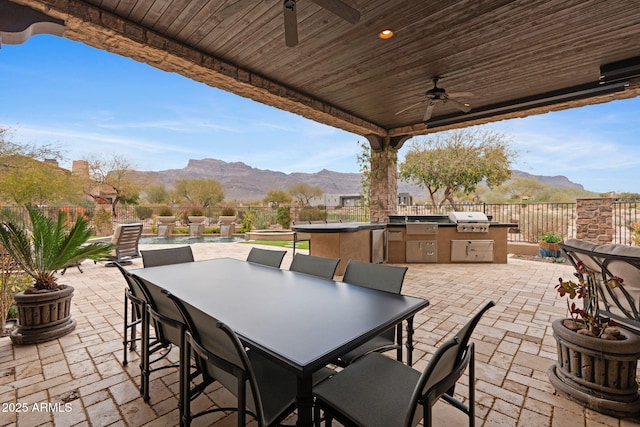 view of patio / terrace with area for grilling, a mountain view, ceiling fan, and an outdoor kitchen