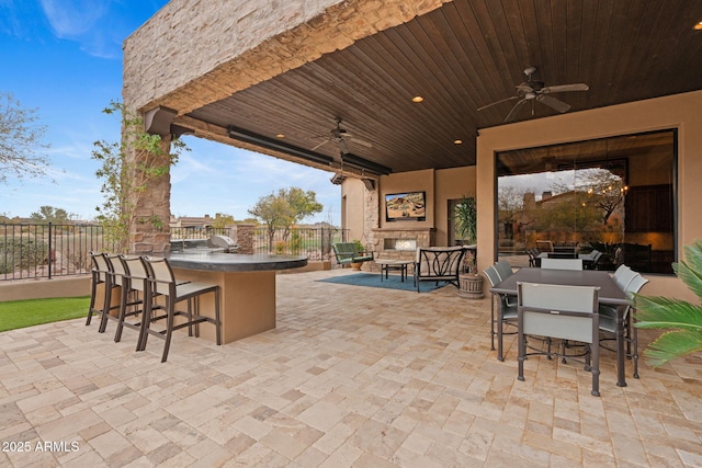 view of patio with ceiling fan, exterior bar, and an outdoor stone fireplace