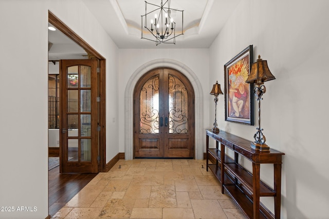 foyer entrance with french doors, a tray ceiling, and a notable chandelier