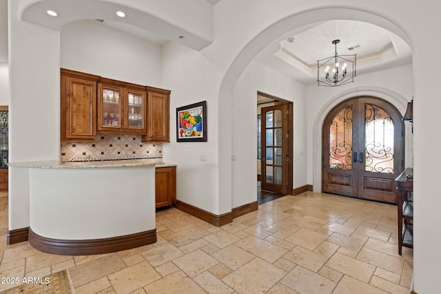 entrance foyer with a chandelier, french doors, a raised ceiling, and a high ceiling