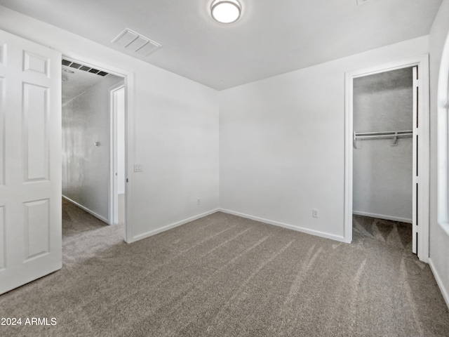 unfurnished bedroom featuring carpet flooring, a walk in closet, and a closet