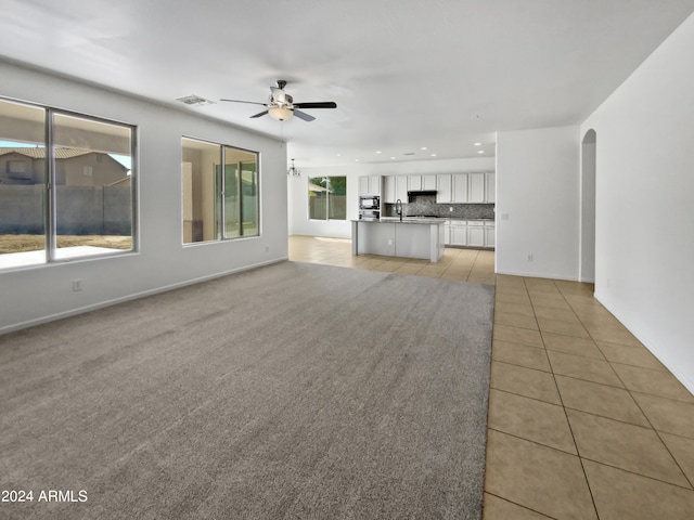 unfurnished living room with ceiling fan, light tile patterned flooring, and sink