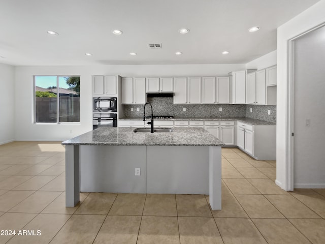 kitchen featuring a kitchen island with sink, stone countertops, and black appliances