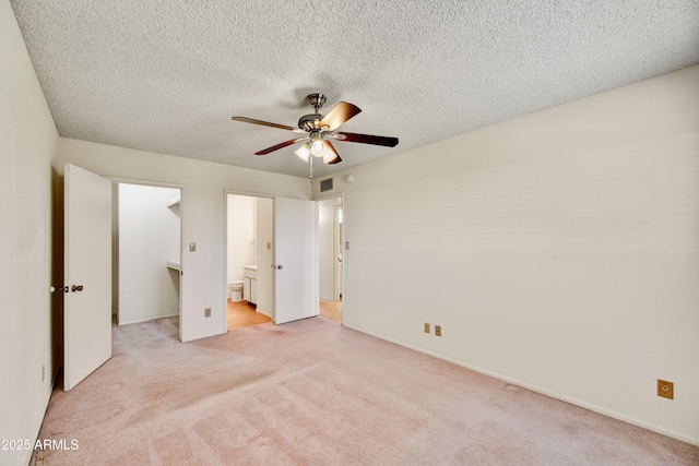 unfurnished bedroom with light colored carpet, ensuite bathroom, baseboards, and a textured ceiling