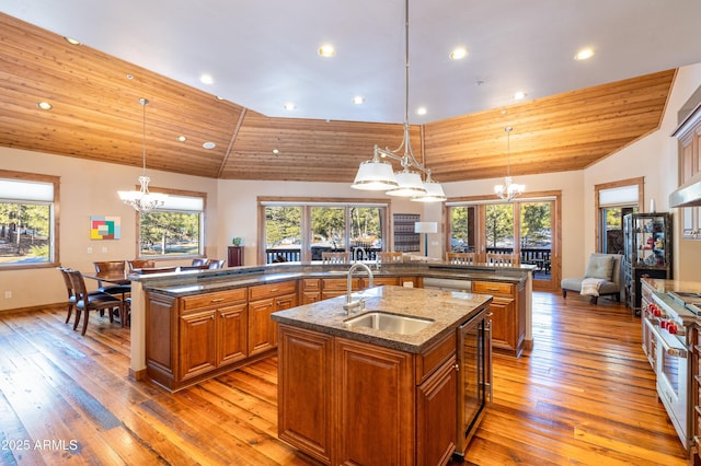 kitchen featuring a kitchen island with sink, a chandelier, brown cabinetry, high end stainless steel range, and a sink