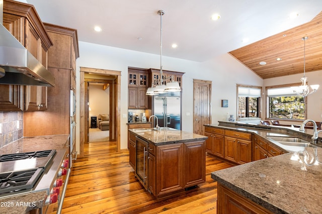 kitchen with premium appliances, a large island with sink, a sink, wall chimney exhaust hood, and brown cabinets