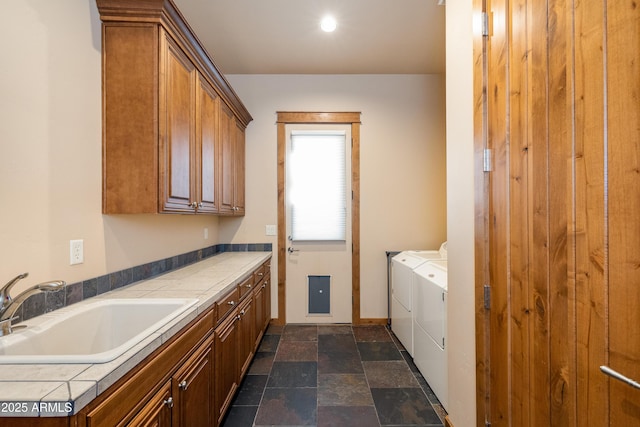 clothes washing area with baseboards, stone tile floors, separate washer and dryer, cabinet space, and a sink