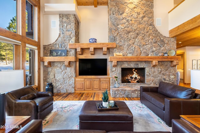 living room with beam ceiling, a stone fireplace, wooden ceiling, a towering ceiling, and wood finished floors