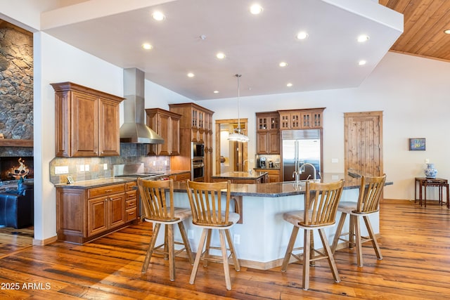 kitchen with a large island, a kitchen breakfast bar, wall chimney exhaust hood, and built in appliances