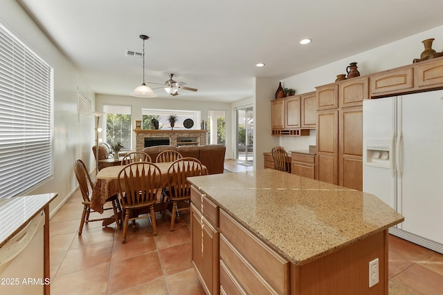 kitchen with decorative light fixtures, white appliances, ceiling fan, light stone countertops, and a kitchen island