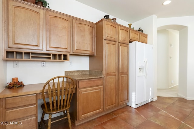 kitchen featuring white refrigerator with ice dispenser, built in desk, and dark tile patterned flooring