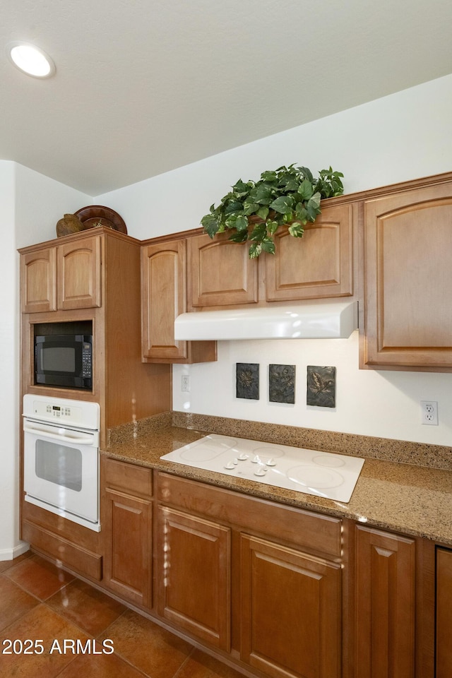 kitchen with white appliances, dark tile patterned floors, and light stone counters