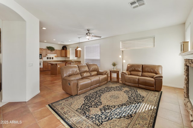 tiled living room featuring ceiling fan and a stone fireplace