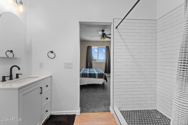 bathroom with a tile shower, ceiling fan, wood-type flooring, and vanity