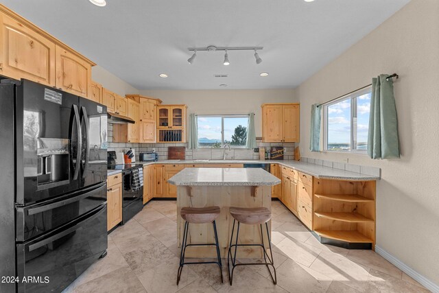 kitchen with decorative backsplash, a kitchen island, a breakfast bar, black appliances, and sink