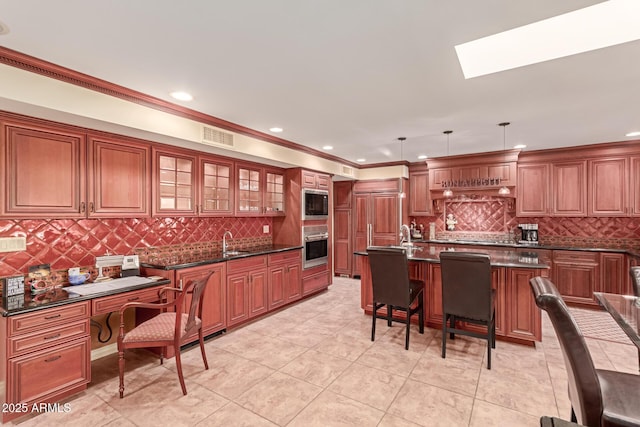 kitchen with an island with sink, dark stone countertops, pendant lighting, and oven