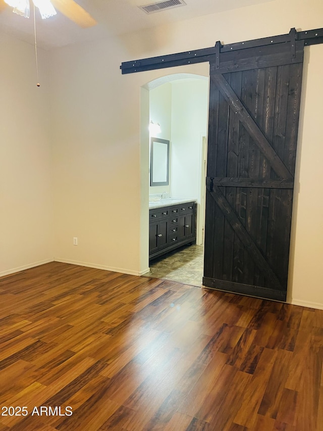 empty room with a sink, a barn door, baseboards, and wood finished floors