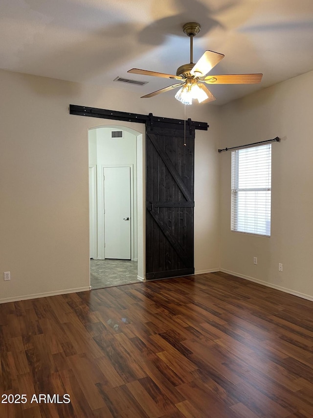 unfurnished room with visible vents, a barn door, ceiling fan, wood finished floors, and baseboards