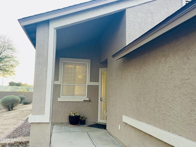 entrance to property featuring a patio area, fence, and stucco siding