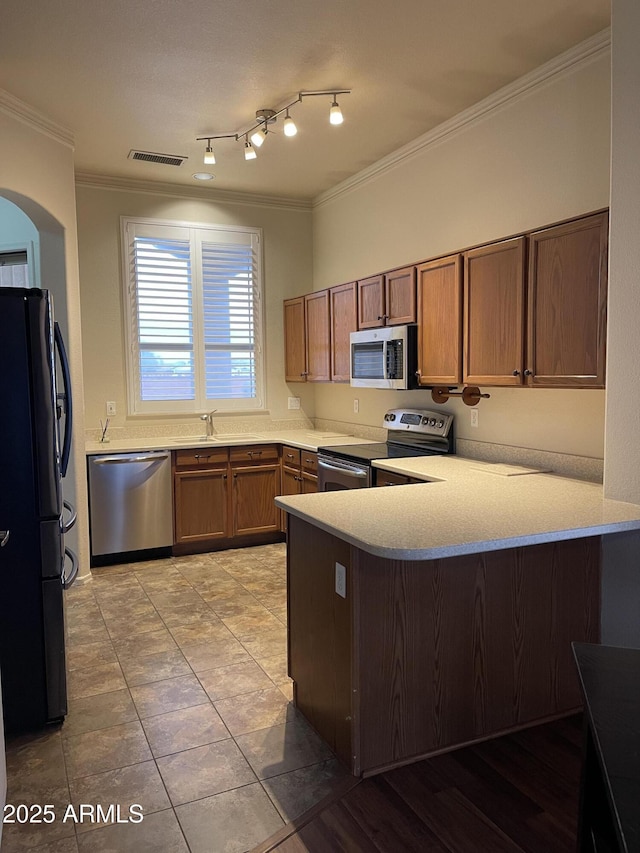 kitchen featuring a peninsula, light countertops, appliances with stainless steel finishes, brown cabinets, and crown molding