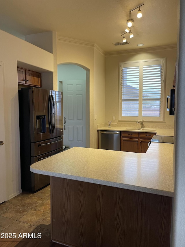 kitchen featuring a peninsula, a sink, light countertops, ornamental molding, and appliances with stainless steel finishes