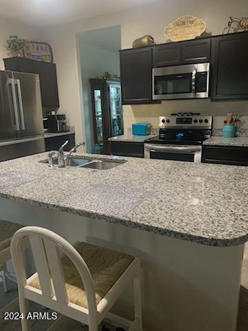 kitchen featuring a kitchen island with sink, a kitchen breakfast bar, sink, appliances with stainless steel finishes, and light stone counters