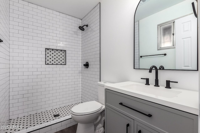 bathroom with vanity, toilet, and tiled shower