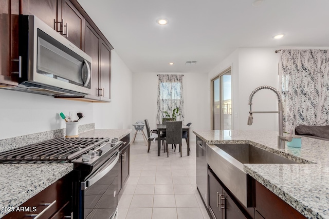 kitchen with sink, light tile patterned floors, light stone counters, stainless steel appliances, and dark brown cabinets