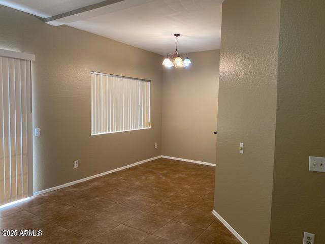 empty room featuring a chandelier and baseboards