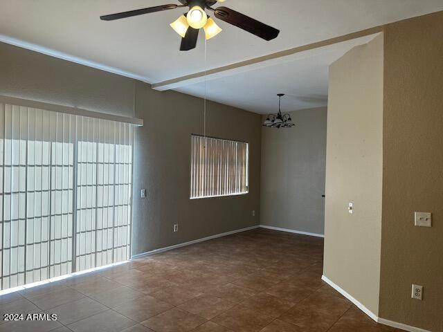 empty room featuring beamed ceiling, baseboards, and ceiling fan with notable chandelier