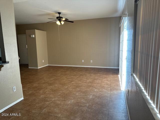 spare room featuring ceiling fan, baseboards, and dark tile patterned flooring