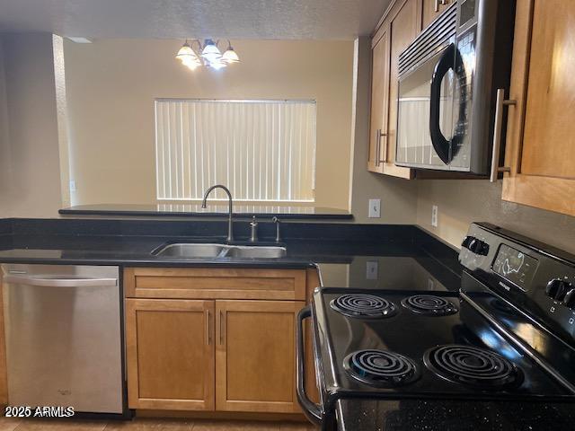 kitchen with dark countertops, appliances with stainless steel finishes, brown cabinetry, and a sink