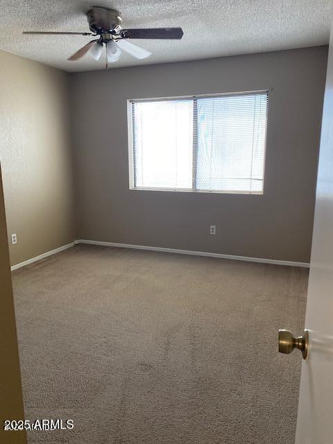 carpeted spare room featuring ceiling fan, a textured ceiling, and baseboards