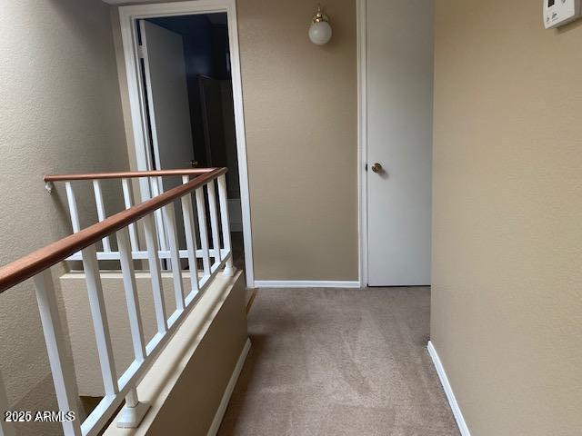 hall featuring carpet floors, an upstairs landing, a textured wall, and baseboards